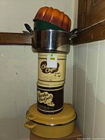 Stack showing yellow casserole, two Charles Chips tins, stainless pot and orange Bundt pan