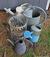 Grouped view of four watering cans and metal birdcage outdoors