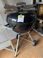 Full view of Weber charcoal kettle grill on stand with utensils on lid