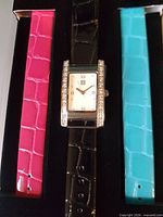Watch with black strap between pink and turquoise straps