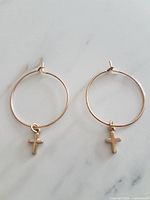 pair of gold-tone hoop earrings with cross charms displayed flat