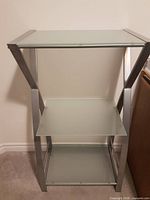 Front view of one shelving unit showing three frosted glass shelves and metal frame