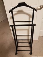 Full front view of black valet stand showing hanger top, rails, casters.