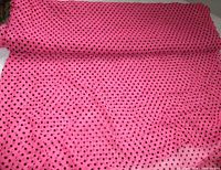 Roll of hot pink fabric with black polka dots unrolled over surface