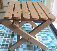 Angle view of wooden folding stool showing slatted top and X-frame legs