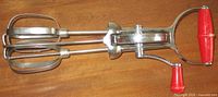 Full view of stainless hand egg beater showing both beaters and red handle