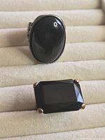 Two silver-tone rings with black stones, one oval cabochon, one rectangular faceted