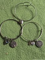 Three silver-tone expandable charm bracelets laid out on green surface