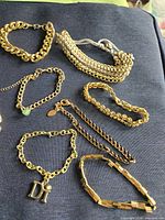 Group of seven gold-tone chain link bracelets and one multi-strand chain necklace laid out on dark fabric