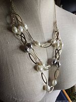 Full view of necklace on mannequin showing silver-tone chain, gold-tone oval links, white and grey beads
