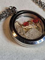 Round glass locket pendant on silver-tone chain containing sand, sea glass, red beads, anchor charm