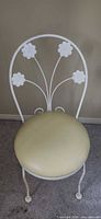 Front view of white metal chair with floral back and yellow vinyl seat