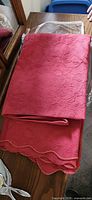 Folded burgundy cotton bed cover showing floral embossed pattern and scalloped edge