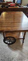 Full view of wooden tea cart with drop-leaf sides, handle, shelf and wheels