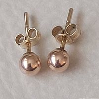 Front view of both gold stud earrings showing spherical design and posts
