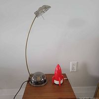Full view of brass gooseneck lamp and red rocket night light on table