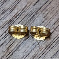 Front view of both gold earring backs on wood surface