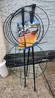 Four metal ring plant supports, two black packaged Quest supports and two green supports leaning against wall