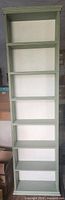 Front view of tall sage green wood bookshelf showing six shelves and white back panel