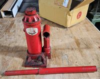 Red hydraulic bottle jack with detachable handle shown on workbench