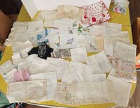Wide view of approximately 50 assorted vintage handkerchiefs laid out on yellow surface