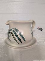 Side view of ceramic gravy boat showing attached saucer, handle, spout and painted branch motif