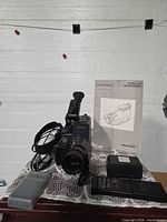 Front view of Nordmende VS3 camcorder with viewfinder, strap, manual, battery pack, and charger visible