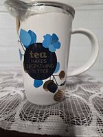 Full view of teacup with handle, graphic, lid wrapped in plastic seated on cup