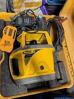 Rotary laser level, remote, power adapter, cables seated in yellow foam case