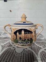 Front view of ceramic lidded sugar dish showing Munich relief and handles