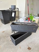 Two black wicker-look planters, metal stand with grey pot visible