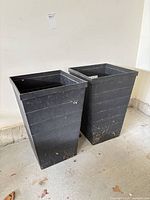 Two black plastic tall planters side by side