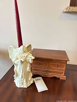 Porcelain angel candle holder with red taper beside wooden jewelry box on table