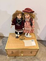 Two porcelain dolls standing on wooden chest