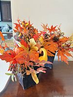 Two artificial fall floral arrangements side by side in black vases