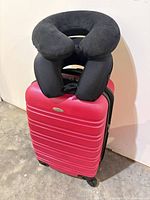 Pink Samsonite carry-on suitcase with two black neck pillows stacked on top