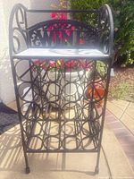 Front view of black wrought-iron wine rack showing bottle slots and top shelf