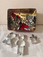 Open tin showing multiple metal and plastic holiday cookie cutters