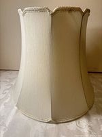 Full side view of ivory empire bell lampshade with scalloped top and braided trim