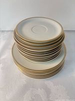 Stack of 20 white porcelain saucers with gold rim