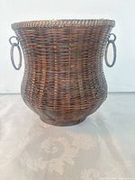 front view of woven wicker basket showing ring handles and hourglass shape