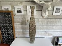 Full frontal view of the tall metal vase showing embossed pattern and overall shape