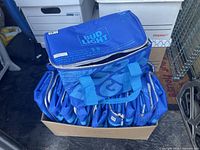 Box containing multiple folded blue Bud Light 6-pack cooler bags with one opened to show logo and zipper