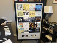 Full view of framed Genesis album covers poster on stand