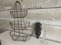Full view of wire basket stand, wooden mask and glass candlestick