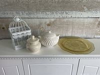Group view of bird cage, ceramic jar, tureen and amber platter on cabinet