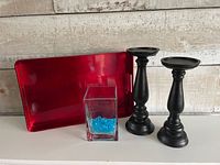 All items together: two black candle holders, red tray, glass vase with blue stones