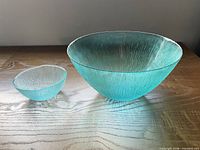 Large and small sea blue textured glass bowls side by side on wood surface