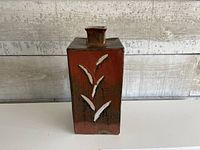 Front view of square reddish-brown pottery vase with white leaf appliqué
