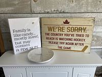 All three items on dresser: sealed clock, wrapped family quote sign, wood hockey quote sign
